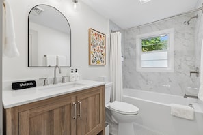 Un bagno moderno con un mobile lavabo bianco, uno specchio grande, un armadietto in legno, un water, una vasca da bagno e una tenda per la doccia.