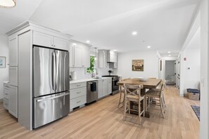 Una cucina moderna con elettrodomestici in acciaio inossidabile, mobili bianchi e un tavolo da pranzo in legno con sedie.