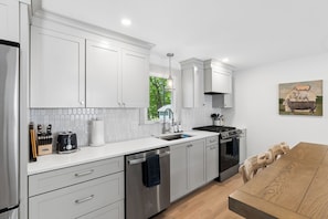 A modern kitchen with white cabinets, stainless steel appliances, and a wooden dining table.