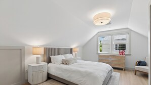 A bedroom with a bed, bedside tables, a window, and a ceiling light. - Luxe 5 Bed/ 3 Bath with Game Room & AC (Yarmouth)
