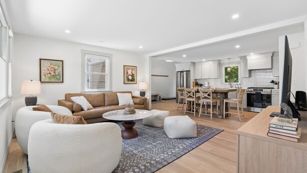 A spacious living room with a sofa, ottoman, and coffee table, a dining area with chairs, and a kitchen with cabinets and appliances. - Luxe 5 Bed/ 3 Bath with Game Room & AC (Yarmouth)