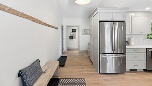A modern kitchen with white cabinets, a stainless steel refrigerator, and a wooden bench. - Luxe 5 Bed/ 3 Bath with Game Room & AC (Yarmouth)