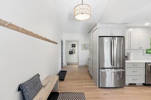 Una cucina moderna con mobili bianchi, un frigorifero in acciaio inossidabile e una panca in legno.