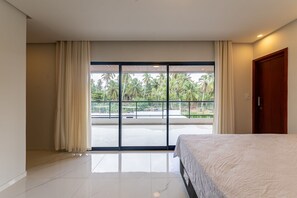 Camera da letto con un letto grande, una porta-finestra su un balcone e vista su palme.