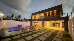 Una casa moderna a due piani con piscina, area salotto esterna e patio ben illuminato.