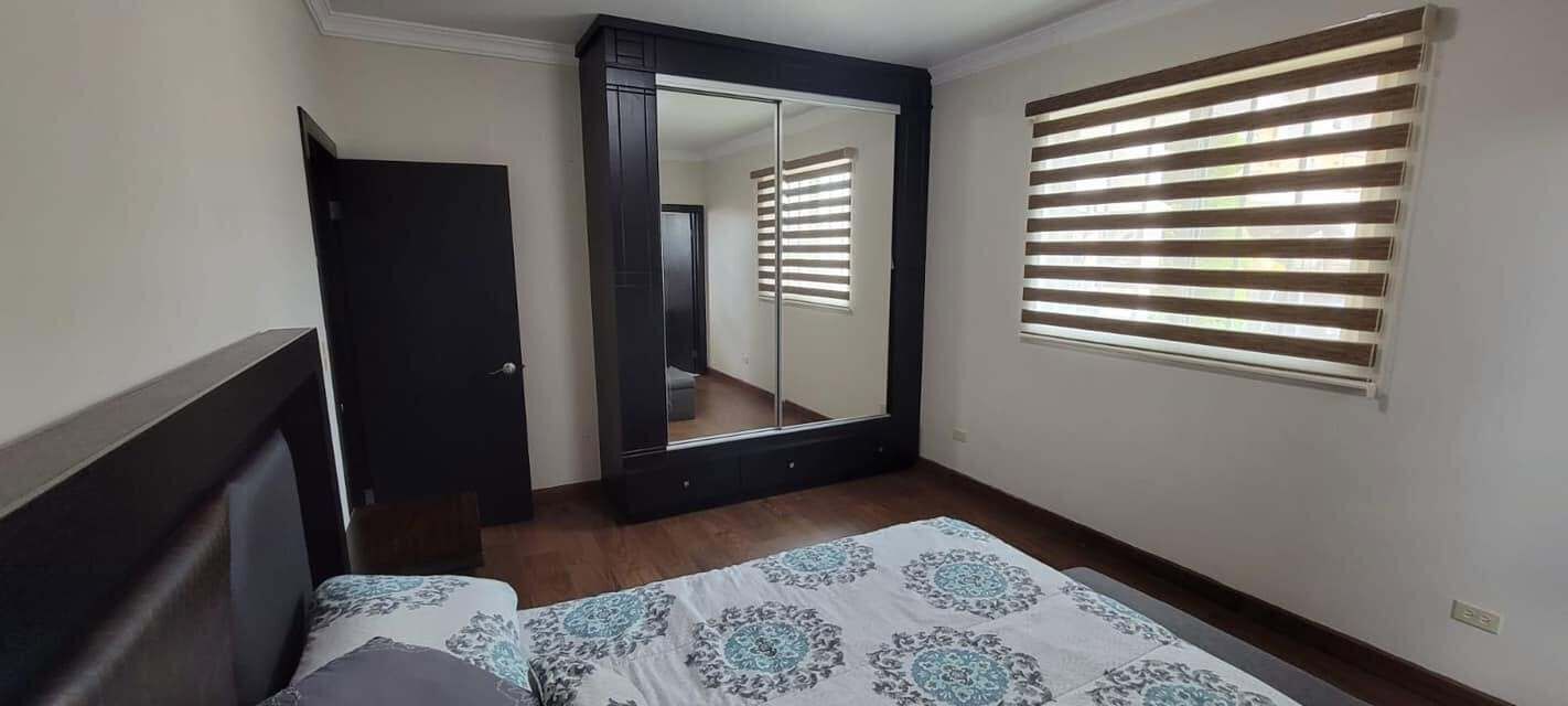 A bedroom with a bed, a wardrobe, a mirror, and a window with blinds.