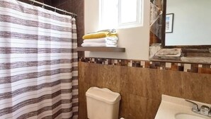 A bathroom with a striped shower curtain, a toilet, a sink, and a towel rack with folded towels. - Villa Privada San Carlos (Ensenada)