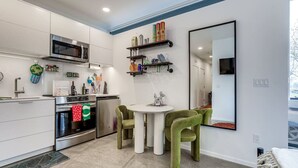 Una cocina moderna con muebles blancos, microondas integrado, horno y comedor con sillas verdes.