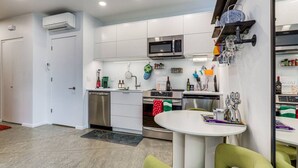 Cocina compacta con microondas, horno y lavavajillas, una pequeña mesa de comedor con sillas y una puerta con una toalla colgada.
