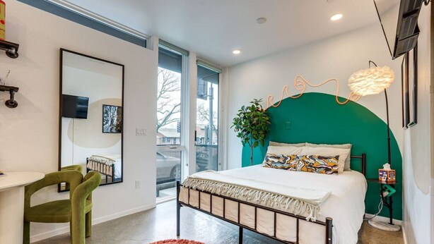 Un dormitorio moderno con cama, escritorio, silla y un ventanal grande.