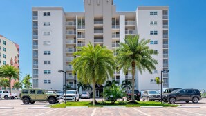 Un edificio de varios pisos con balcones, coches aparcados y palmeras.