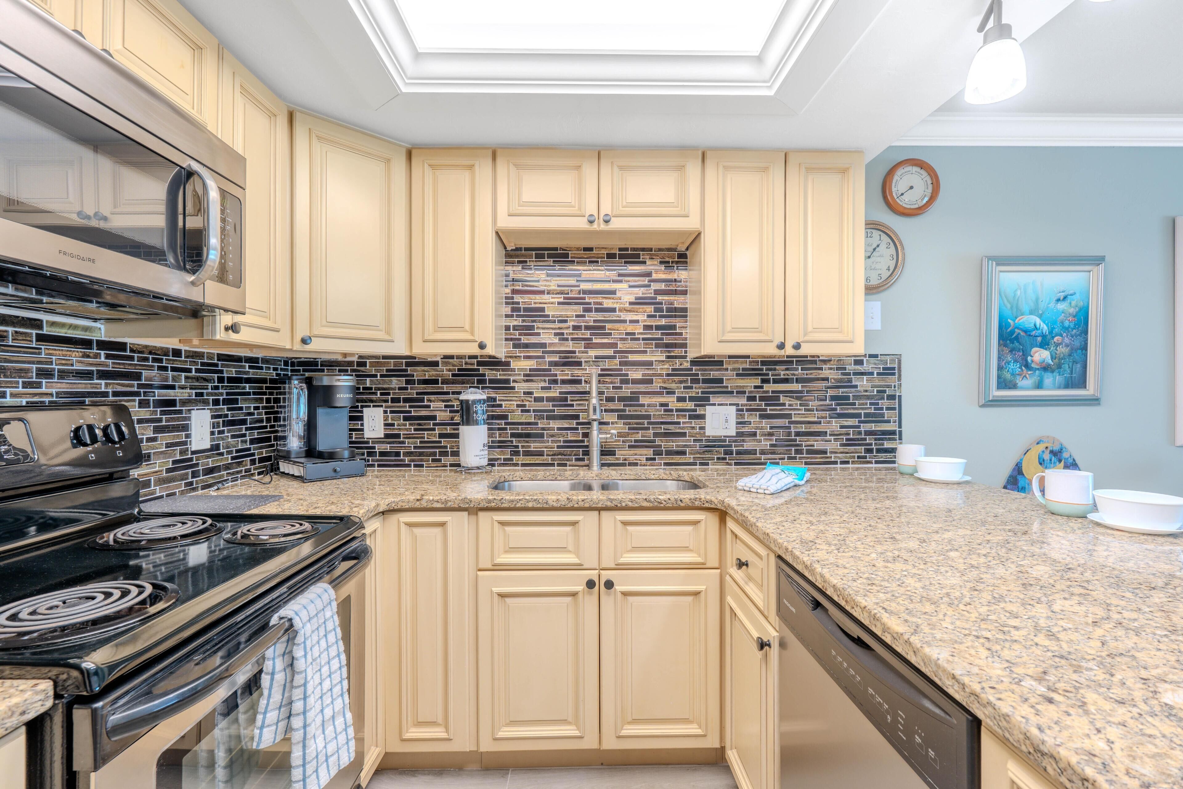 A kitchen with beige cabinets, a black stove, a microwave, and a tiled backsplash.