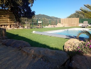 Patio trasero con piscina, césped artificial, rocas y valla de madera.