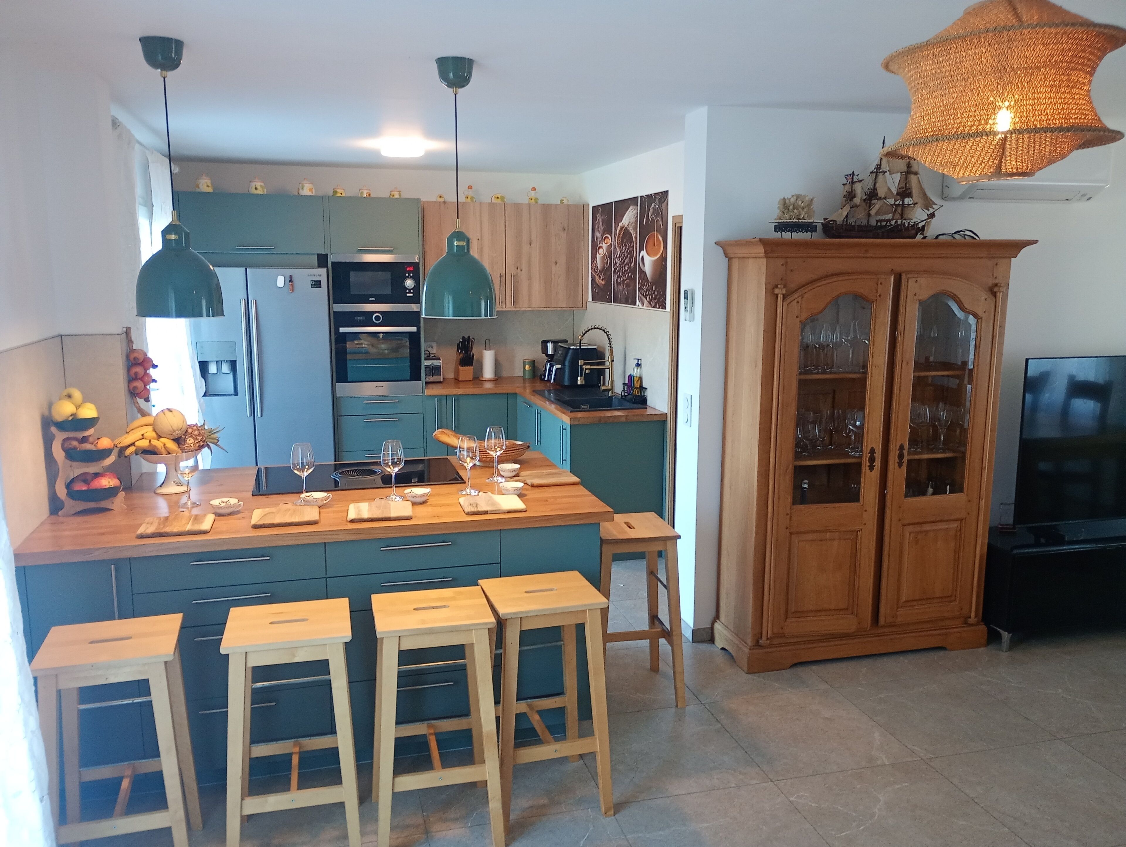 Una cocina moderna con una isla central, taburetes de bar, un armario de madera y un televisor.