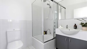 A modern bathroom with a glass-enclosed shower, a toilet, a sink with a mirror, and toiletries. - Sirena by Experience Jervis Bay (Vincentia)
