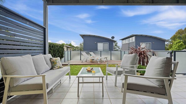 An outdoor patio with a sofa, chairs, and a table. - Sirena by Experience Jervis Bay (Vincentia)