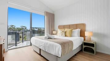 A modern bedroom with a large bed, a nightstand, a lamp, and a view of the outdoors.