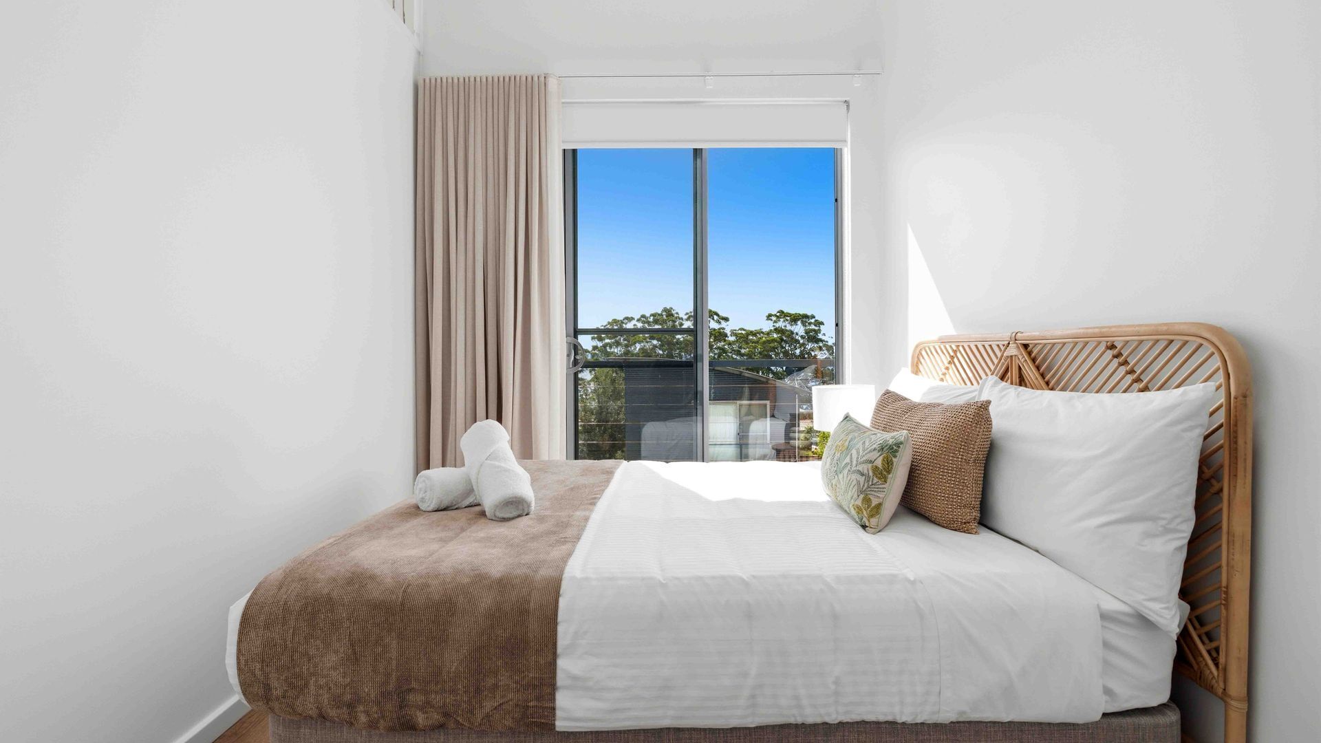 A hotel room with a bed, a window with curtains, and a view of the outside.