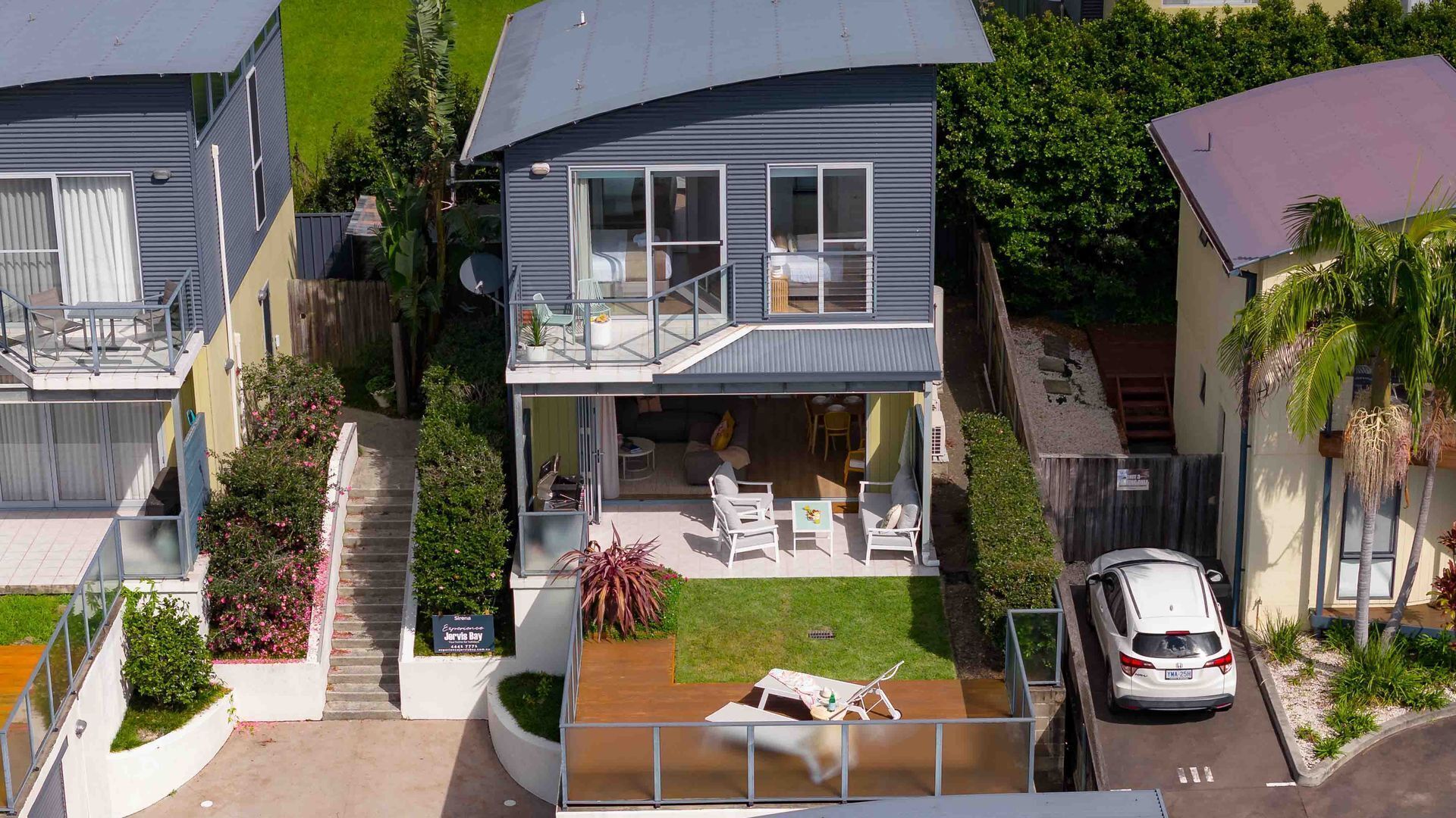 A two-story house with a balcony, a covered patio, and a car parked in the driveway.