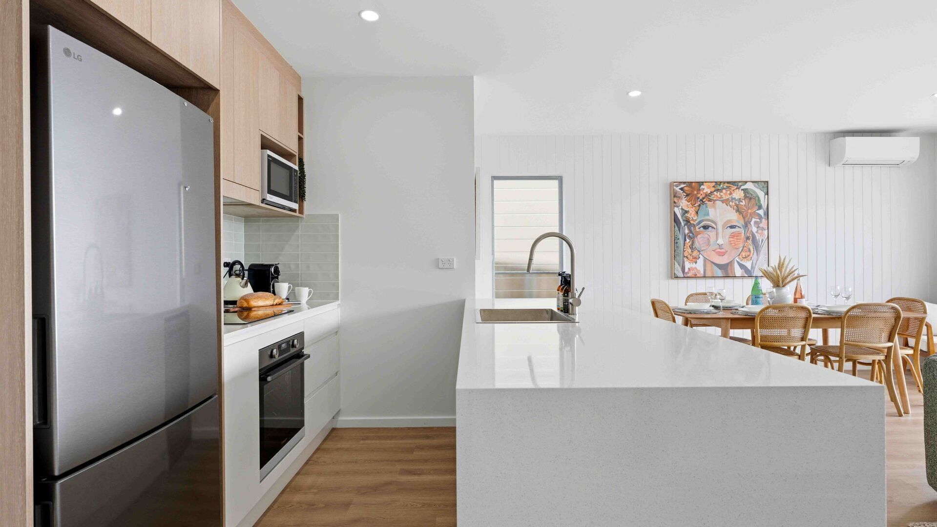 A modern kitchen with a built-in LG refrigerator, microwave, and oven. There's a dining area with a large island and a colorful painting on the wall.