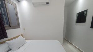 A bedroom with a bed, a window, an air conditioning unit, and a wall-mounted mirror. - hotel castiya (M'diq)