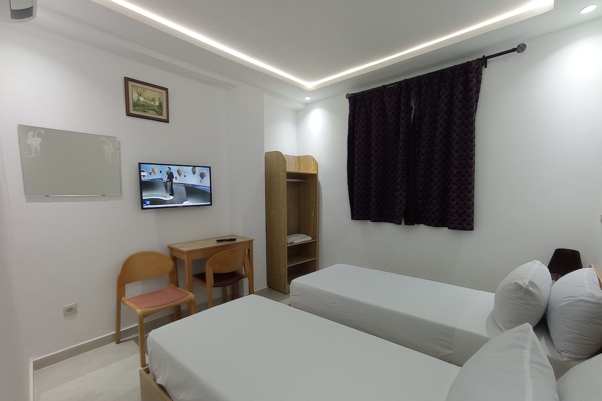 A hotel room with two beds, a desk, a chair, a TV, and a wardrobe.