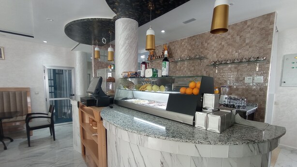 A marble counter with a cash register, a glass display case with fruits, and a bar area with bottles and glasses. - hotel castiya (M'diq)
