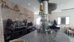 A modern kitchen with a coffee machine, a glass display case, and a dining area with a table and chairs. - hotel castiya (M'diq)