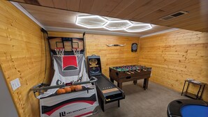 A room with a basketball hoop, foosball table, and a pool table.