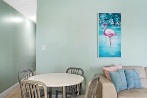 A dining area with a round table and chairs, a light blue wall, and a painting of a flamingo. - St. Martin Beachwalk Villas 313 (Destin)