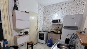 A compact kitchen with a gas stove, microwave, sink, and a small table. - Casa em Ilha Comprida (Ilha Comprida)