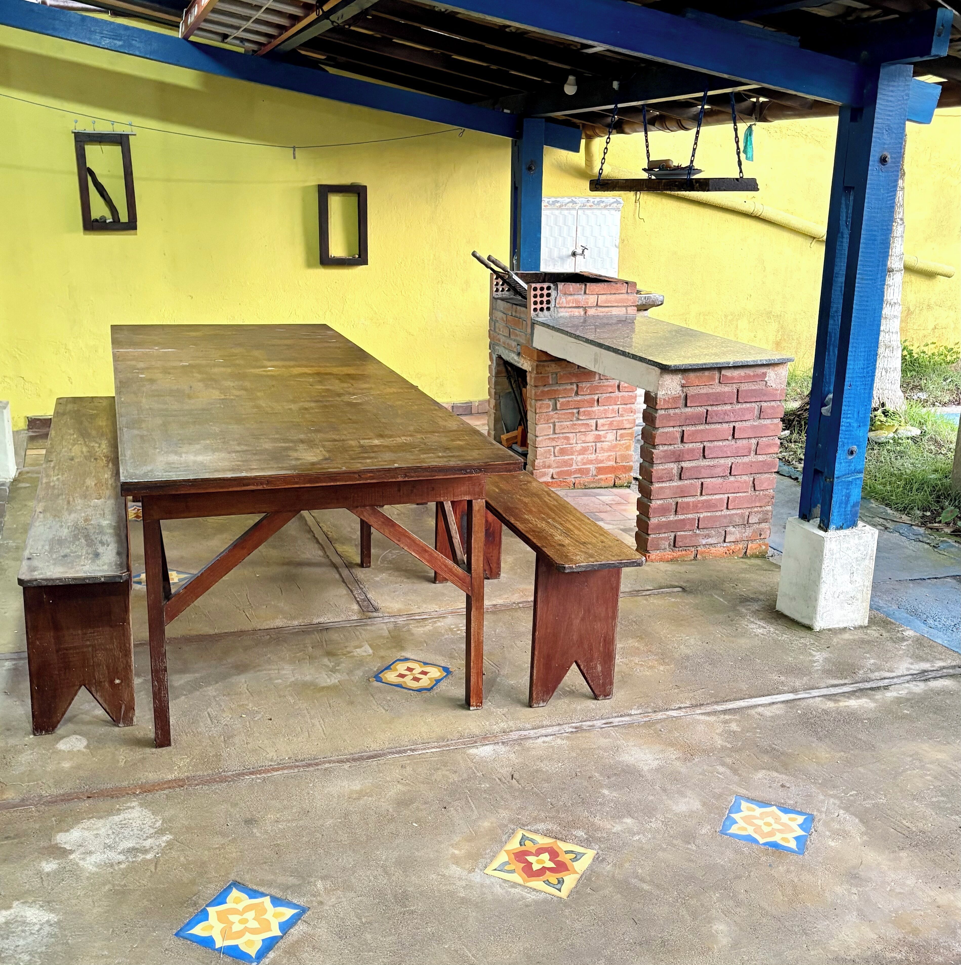 A wooden table with benches, a brick oven, and a yellow wall with a blue ceiling.