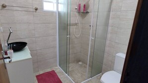 A bathroom with a glass-enclosed shower, a toilet, and a sink with a basin and faucet. - Casa em Ilha Comprida (Ilha Comprida)