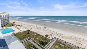A beach view from a hotel balcony with a pool, beach umbrellas, and a wooden deck. - Seascape Towers 624 (New Smyrna Beach)