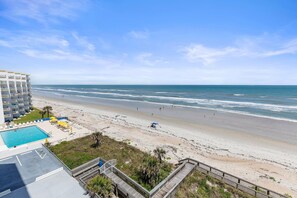 A beach view from a hotel balcony with a pool, beach umbrellas, and a wooden deck. - Seascape Towers 624 (New Smyrna Beach)