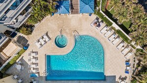 A large swimming pool surrounded by lounge chairs and sunbeds, with a circular hot tub in the center. - Seascape Towers 624 (New Smyrna Beach)