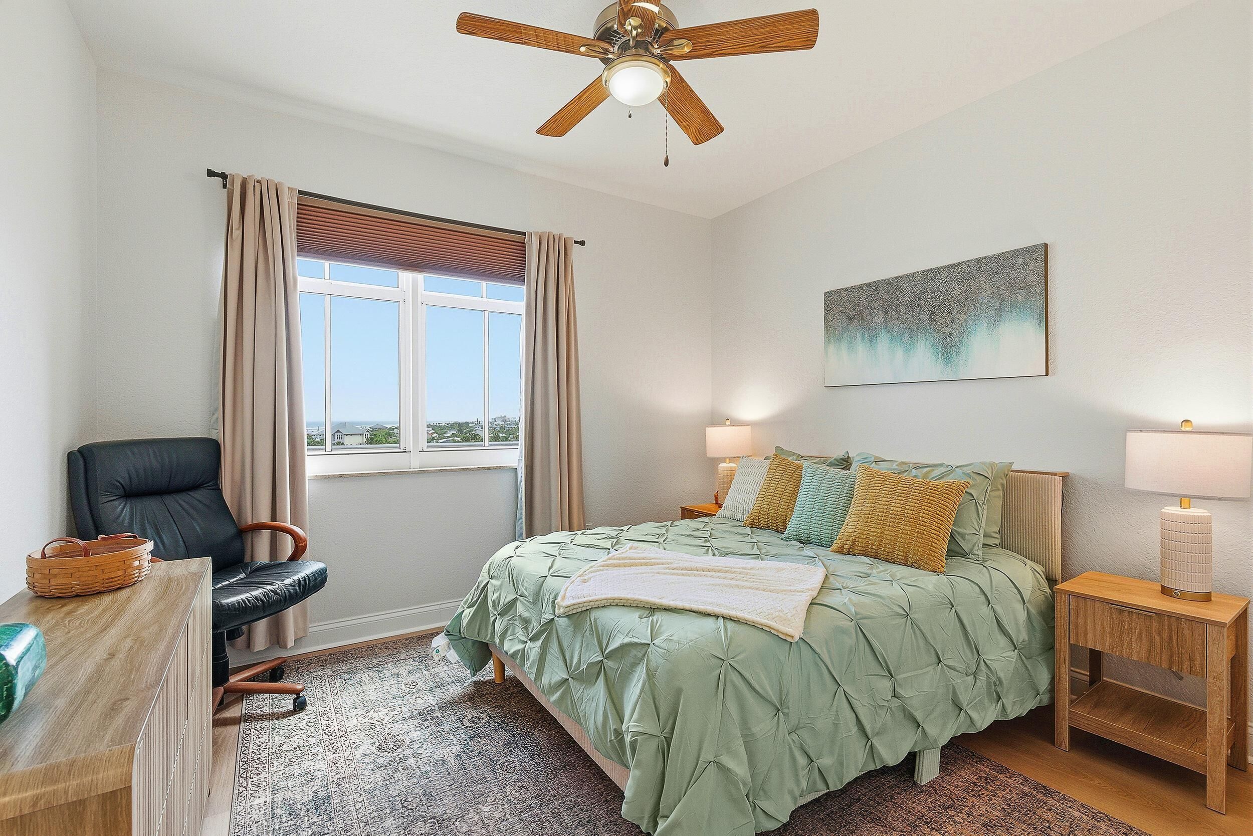 Une chambre à coucher comprenant un lit, une chaise, un bureau, une lampe et un ventilateur de plafond.