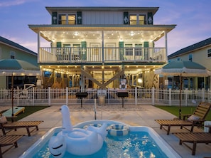Ein zweistöckiges Haus mit Balkon, Schwimmbecken mit Liegestühlen und einem eingezäunten Deckbereich.