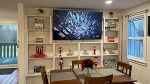 Ein Essbereich mit an der Wand montiertem Fernseher, einem Tisch mit Stühlen sowie Regalen mit Büchern und Dekoration.