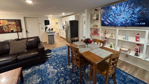 Ein Wohnzimmer mit Sofa, Couchtisch und Fernseher. Es gibt einen Essbereich mit Tisch und Stühlen. Der Raum hat weiße Wände und einen blauen Teppich.