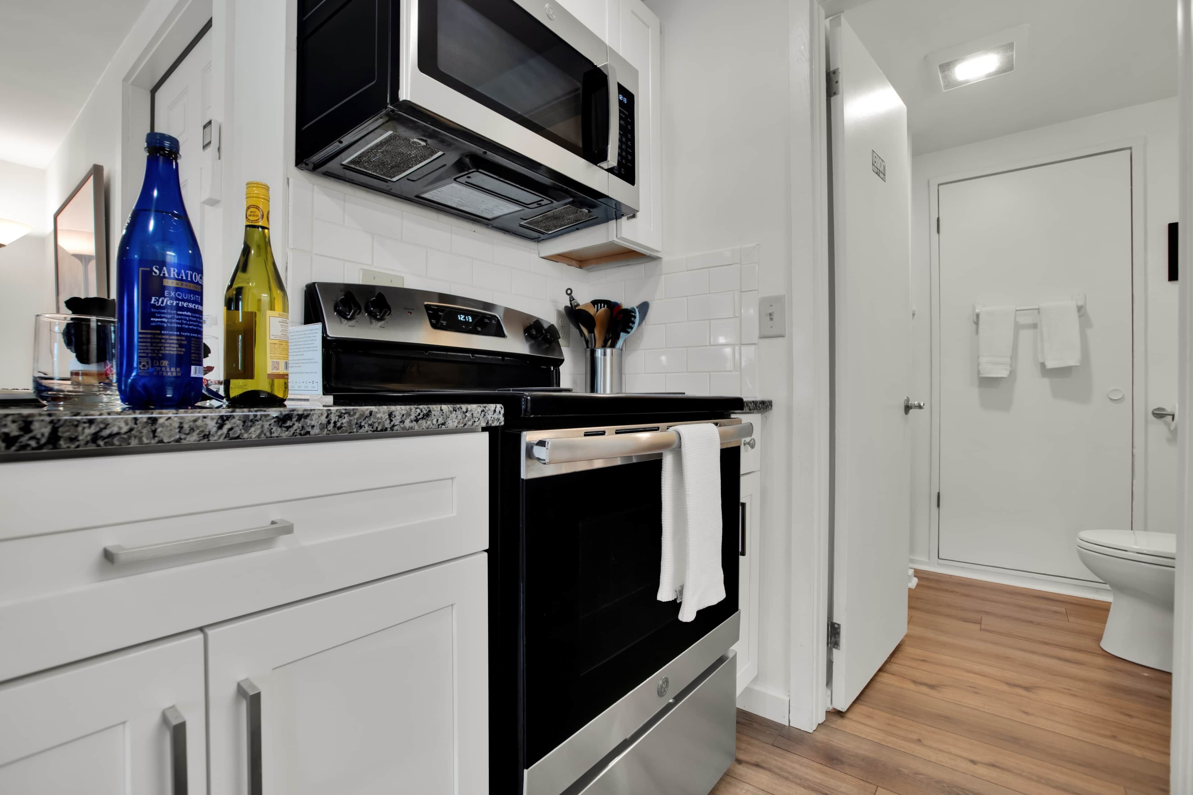 A modern kitchen with a built-in microwave, oven, and stove. There are wine bottles on the counter and a towel hanging on the oven handle.