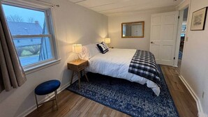 Ein Schlafzimmer mit einem Bett, Nachttischen, einem Fenster, einem Spiegel und einer Tür.