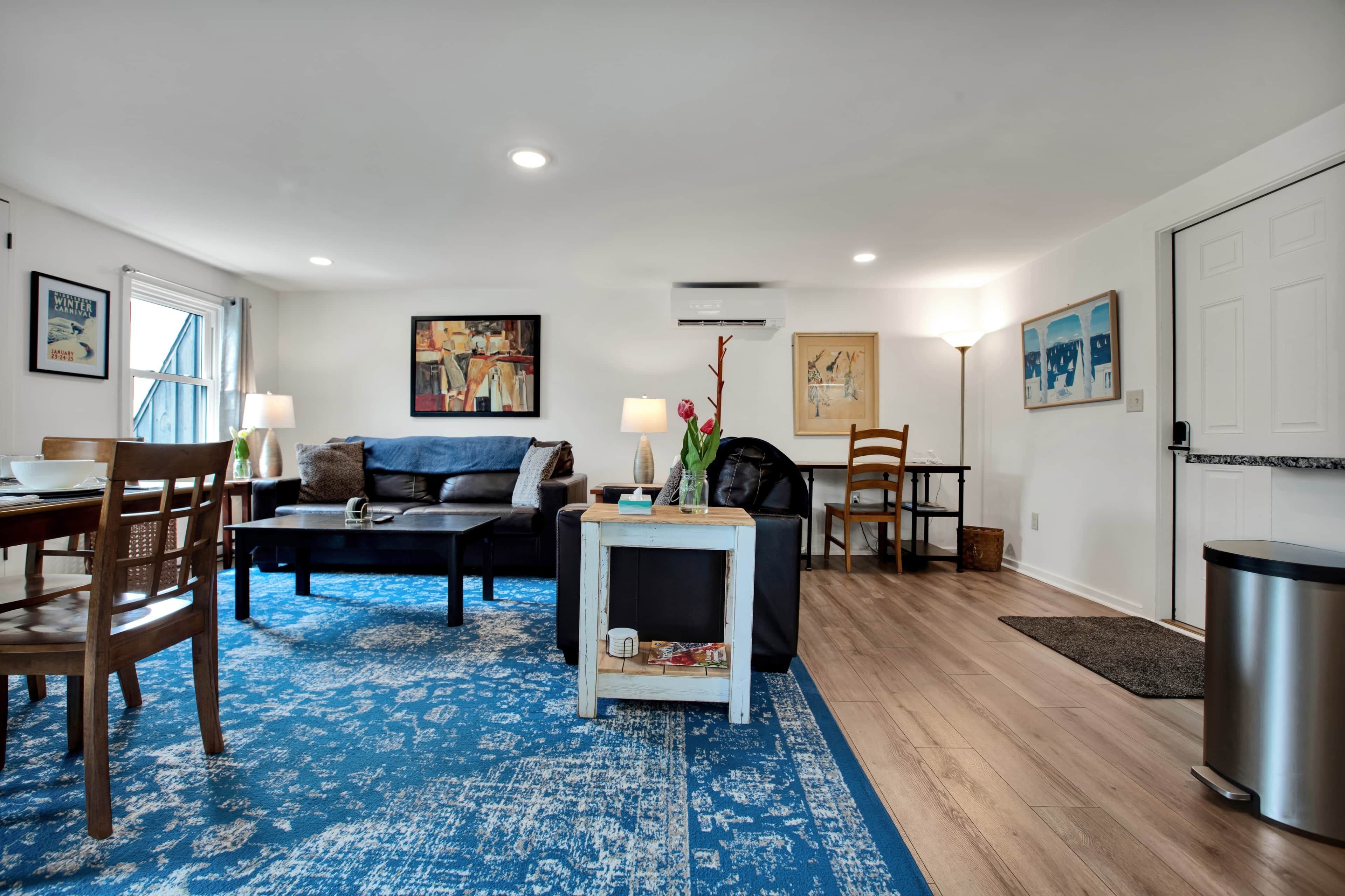 A living room with a blue patterned rug, a sofa, a coffee table, and a dining area with chairs and a table.