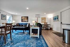 Un salon avec un tapis à motifs bleus, un canapé, une table basse et un coin repas comprenant des chaises et une table.