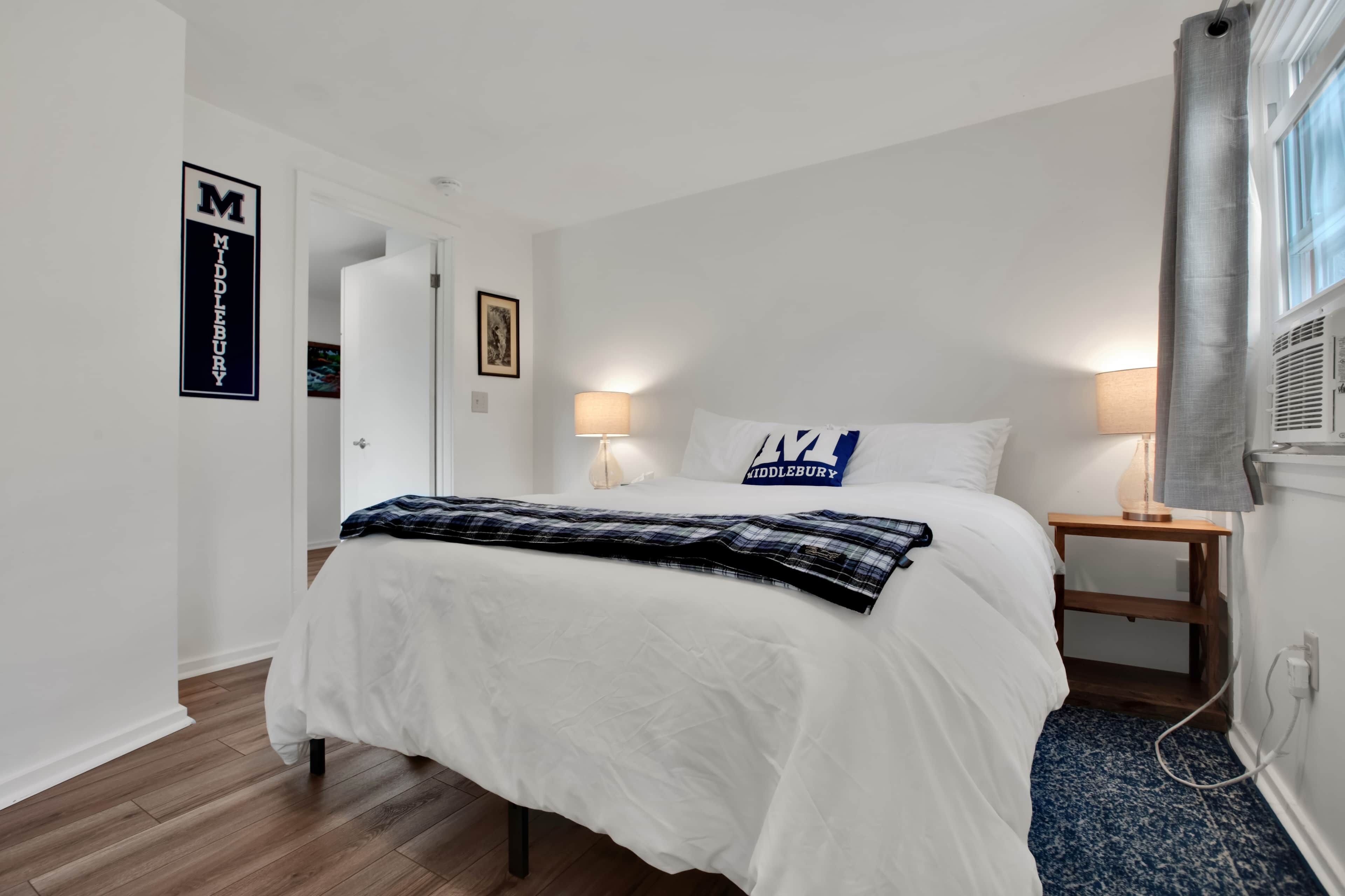 Een slaapkamer met een bed, twee nachtkastjes, een lamp, een fotolijst en een raam met gordijnen.