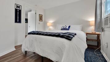 Een slaapkamer met een bed, twee nachtkastjes, een lamp, een fotolijst en een raam met gordijnen.
