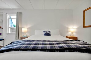 Et hotelværelse med en stor seng, to sengeborde med lamper, et vindue med gardiner og et spejl på væggen.