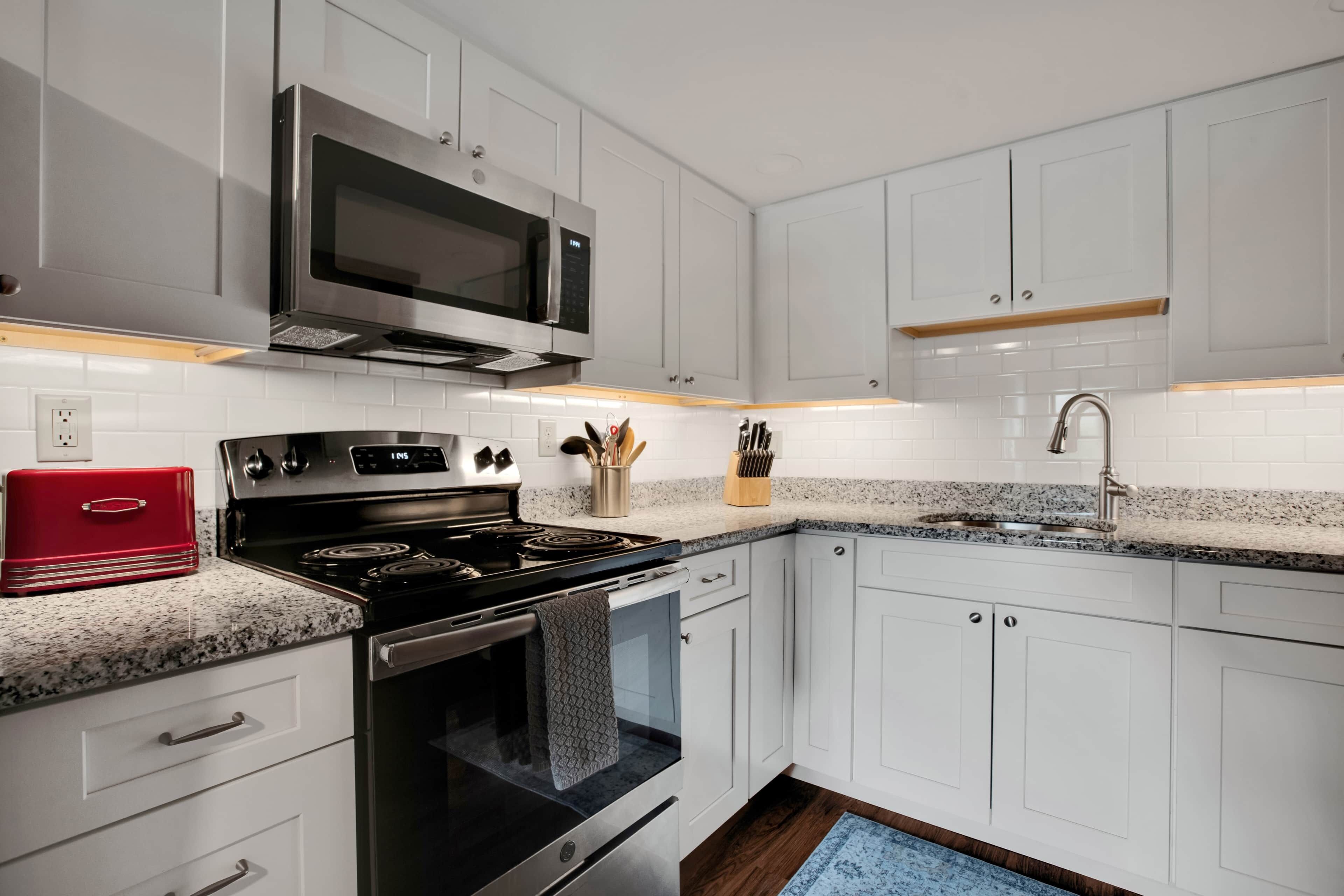 A modern kitchen with white cabinets, a stainless steel stove, a microwave, and a granite countertop.