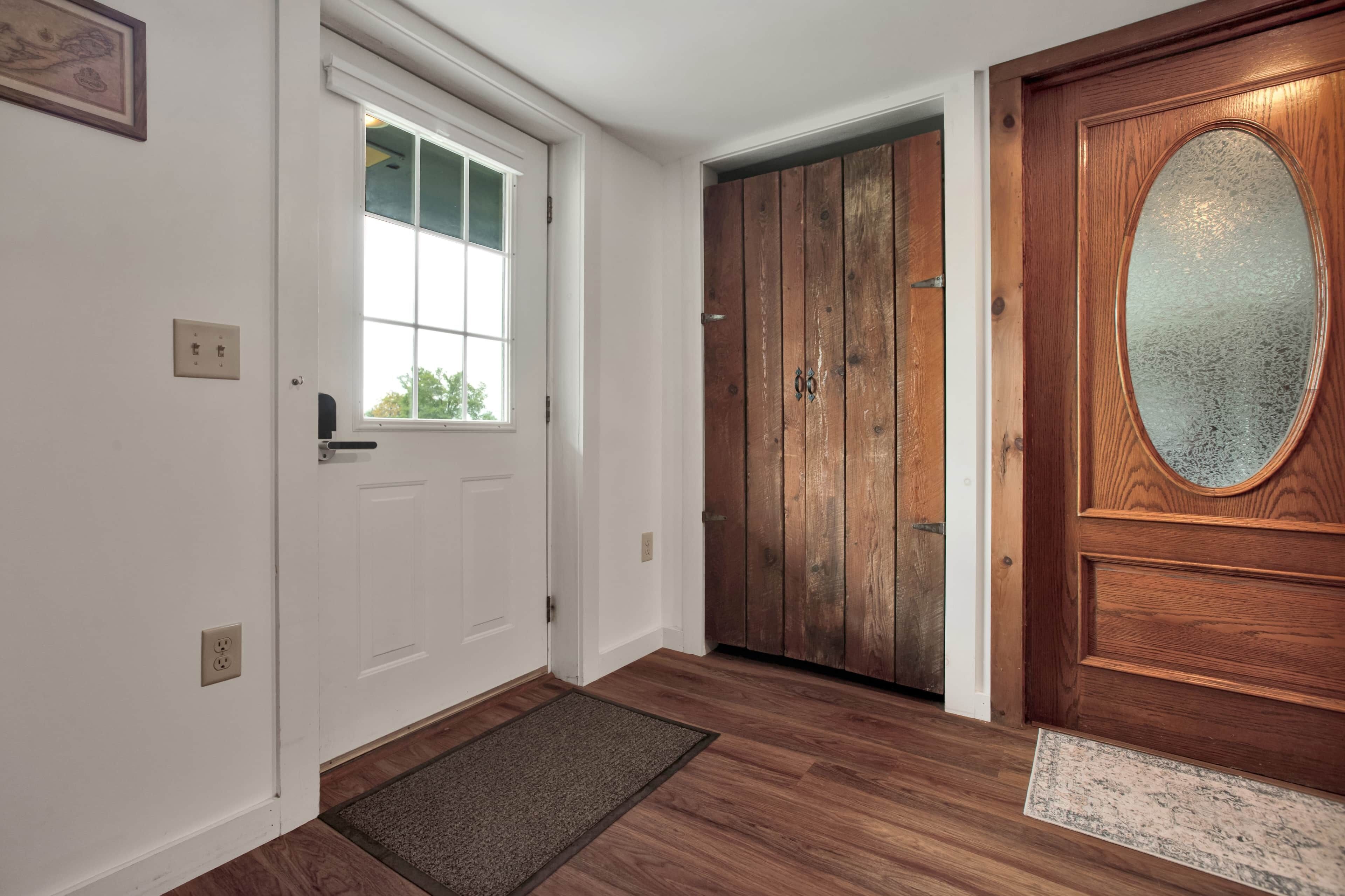 Un pasillo con una puerta blanca, una ventana y una puerta de madera con un panel de vidrio.