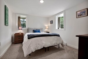 Ein Schlafzimmer mit einem Bett, zwei Nachttischen, einer Kommode und zwei Fenstern.